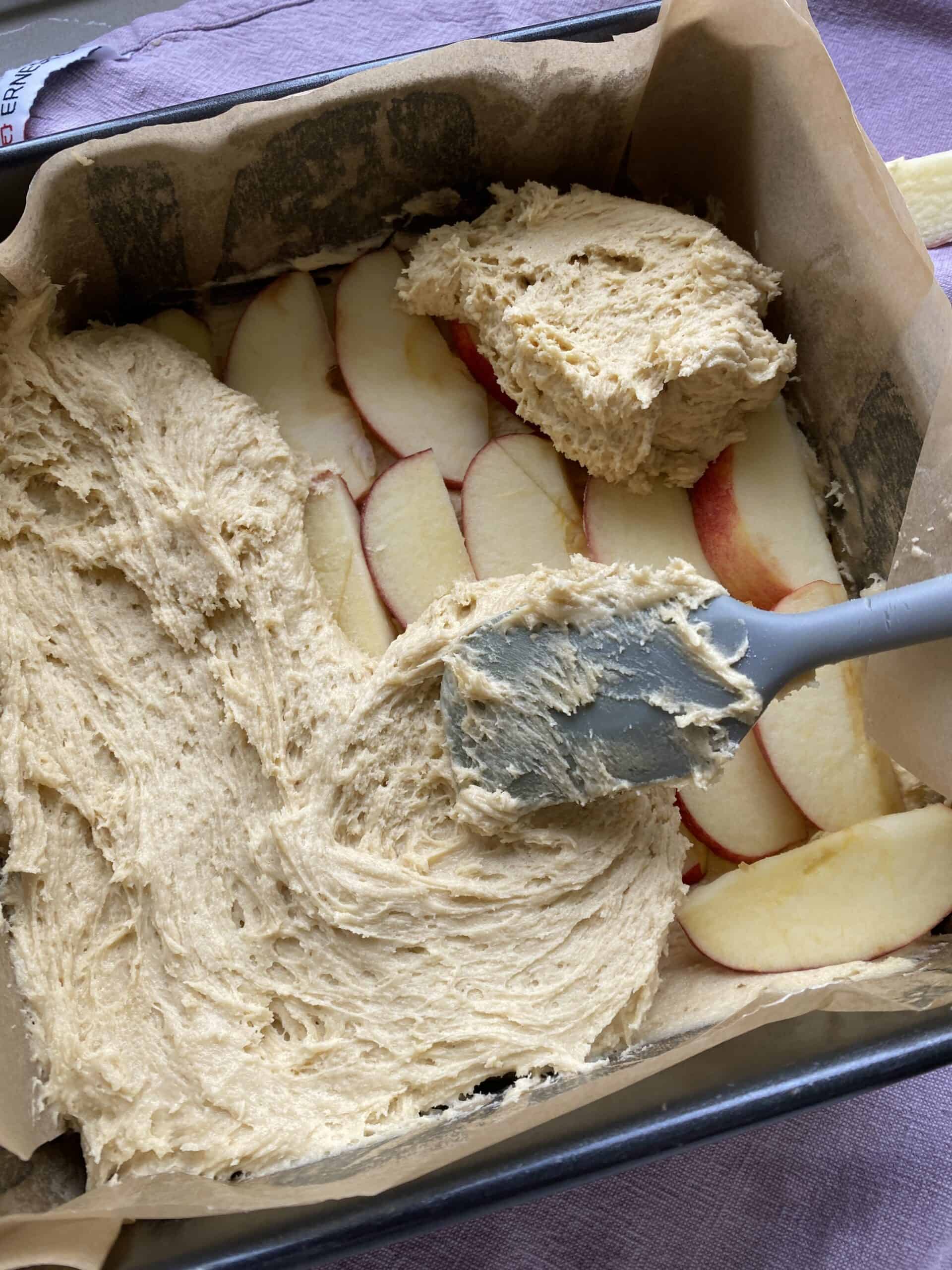 Cake batter and slices of apple in a baking tin.