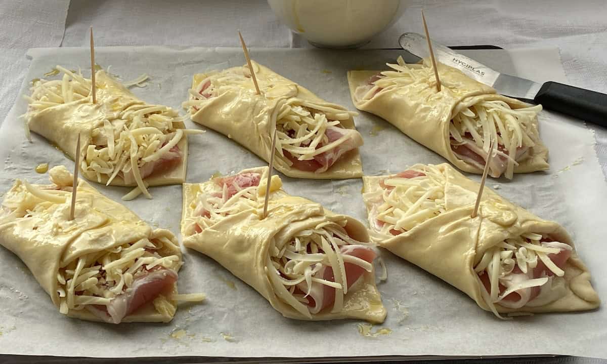 Unbaked cheese and bacon turnovers on a baking tray.